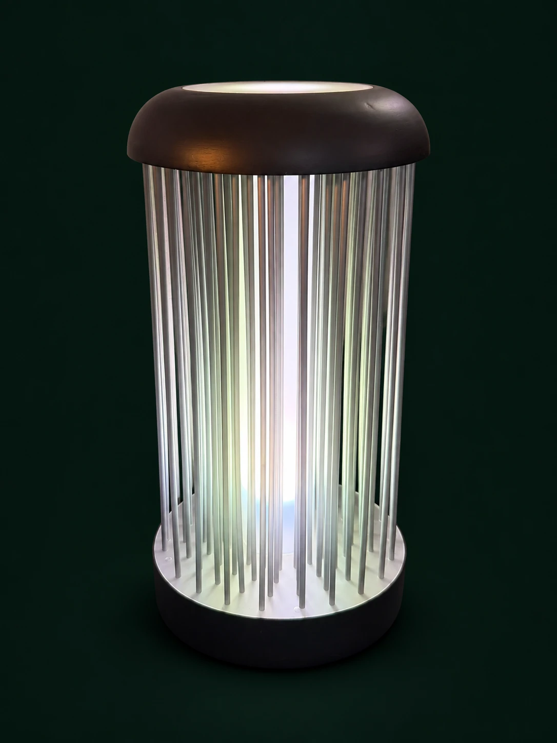 Hohe runde Lampe mit feinen senkrechten Stäben, dunklem gewölbtem Oberteil und weiß leuchtendem Kern