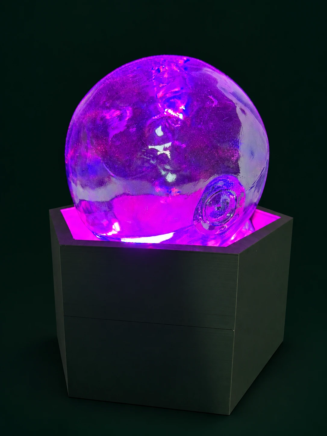Transparente Kugel mit violettem Licht auf einem dunkelgrünen kubischen Sockel